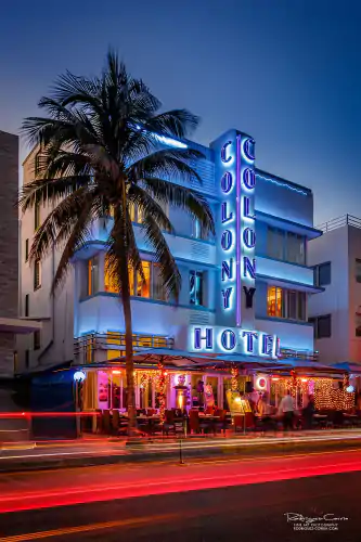 Red, vehicle light steaks in this long exposure of the Colony Hotel in Miami Beach showing the blue neon sign and a palm tree in front.