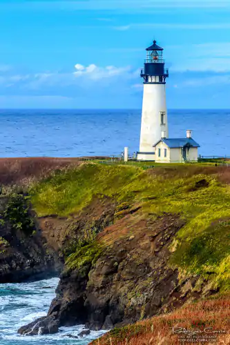 Yaquina Head lighthouse on a cliff with green vegetation and blue sky.