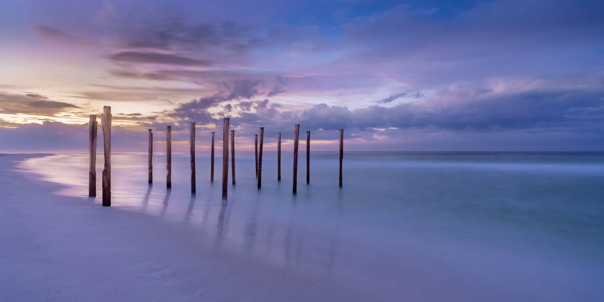 Poles stick out of sand at the beach sunrise.